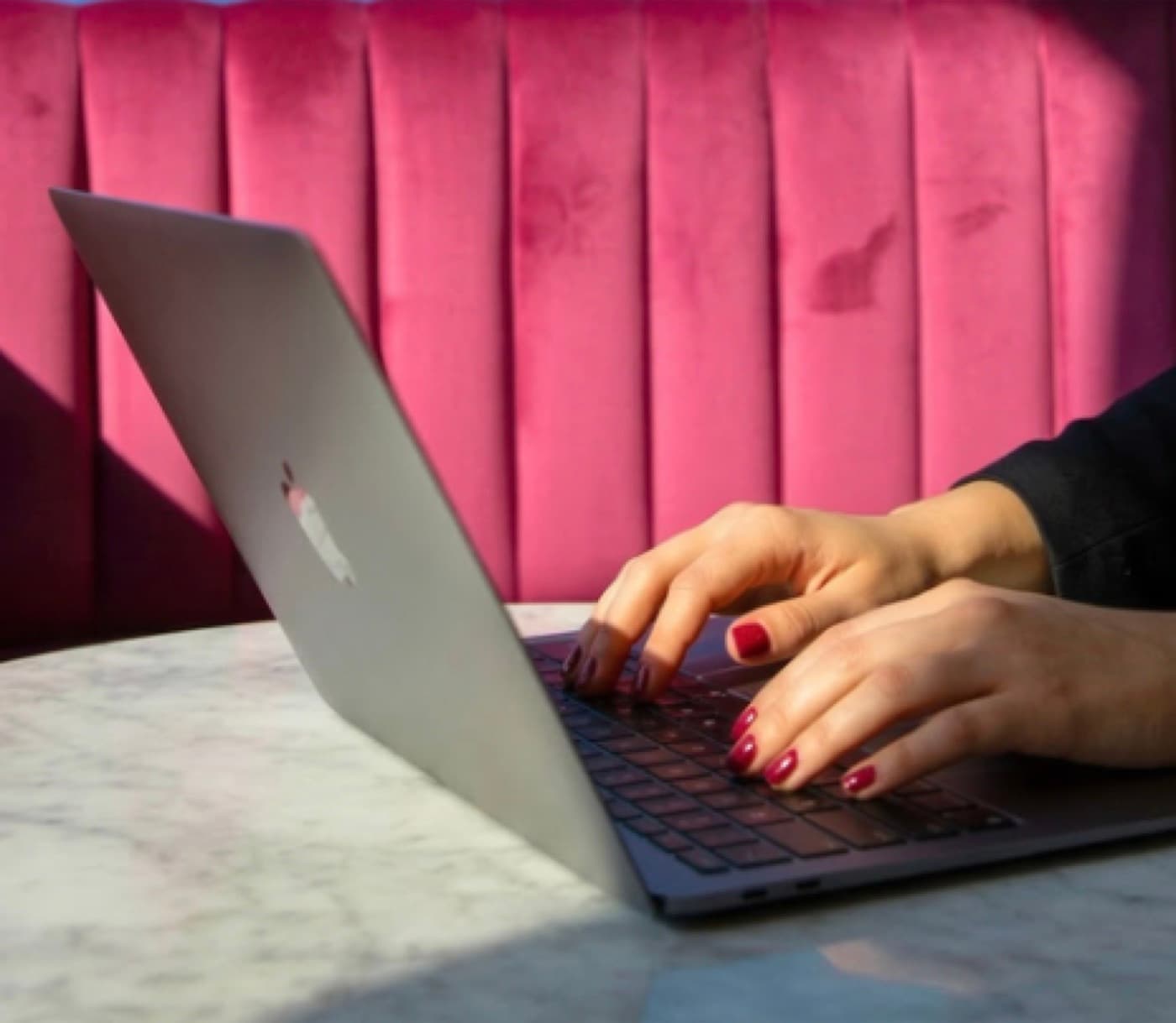 Mani che scrivono su un portatile davanti a una seduta rosa